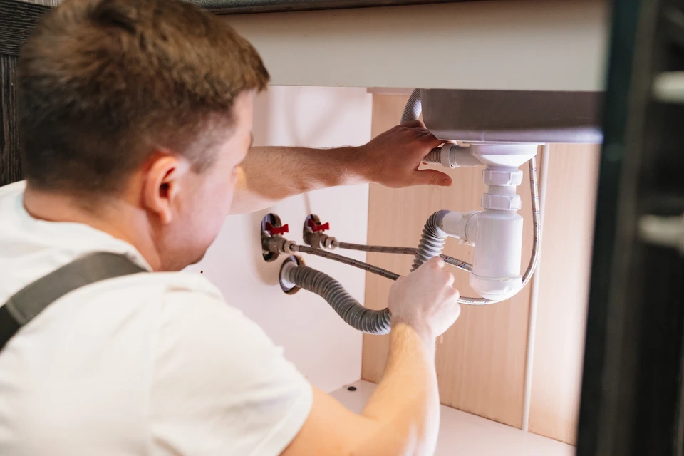 Plombier professionnel en uniforme blanc travaillant sous un évier de cuisine, installant ou réparant la plomberie