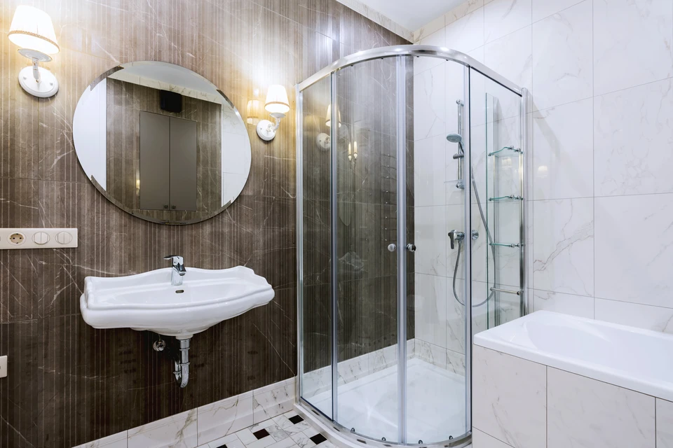 Salle de bain moderne avec douche &agrave; l'italienne vitr&eacute;e, lavabo suspendu blanc, miroir circulaire et baignoire d'angle
