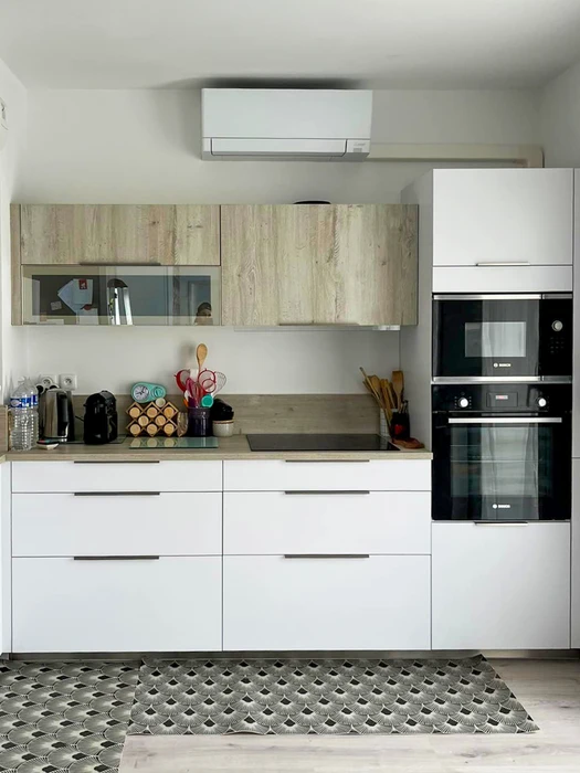 Technicien en noir debout sur échelle double coulisse aluminium, inspectant une unité extérieure de climatisation Mitsubishi fixée en hauteur sur façade enduite rose